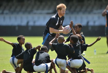 El príncipe Harry, su cuñado y antecesor en el cargo, en un partido de rugby con chicos durante una visita a Sudáfrica en diciembre de 2015.