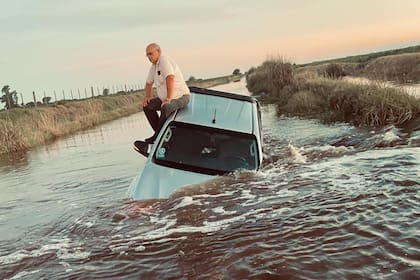El productor Armando Rey sobre el techo de su camioneta, tapada por el agua en un camino rural que une Buenos Aires con Santa Fe