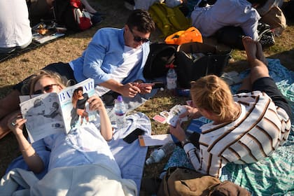 El público lee o juega a las cartas mientras hace la fila para conseguir entradas en el primer día de Wimbledon