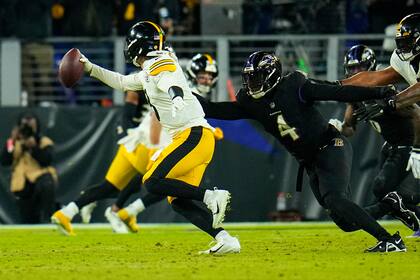 El quarterback Kenny Pickett (8), de los Steelers de Pittsburgh, elude al linebacker Jason Pierre-Paul (4), de los Ravens de Baltimore, antes de enviar un pase para anotación en la segunda mitad del partido de la NFL en Baltimore, Florida, el domingo 1 de enero de 2023. (AP Foto/Julio Cortez)