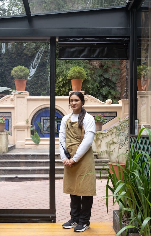 El restaurante funciona en un viejo invernadero y está completamente integrado a su entorno con una terraza rodeada de altísimas palmeras y palos borrachos.