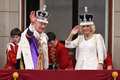 El Rey Carlos III de Gran Bretaña, con la Corona Imperial de Estado, y la Reina Camilla, con una versión modificada de la Corona de la Reina María, saludan desde el balcón del Palacio de Buckingham tras ver el sobrevuelo de la Royal Air Force en el centro de Londres el 6 de mayo de 2023, después de sus coronaciones. (Foto de Oli SCARFF / AFP)
