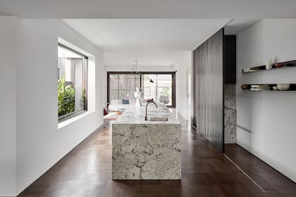El roble del piso de parquet parece trepar por los listones del panel corredizo. La isla, una pieza hecha in situ con cuarcita, Travertino y granito, toma el centro de la escena. El uso de la luz y el detalle, una muestra del aprecio del equipo de diseñadores por la arquitectura japonesa.