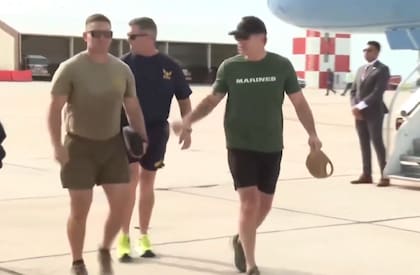 El secretario de Defensa camina junto a dos miembros de la marina estadounidense. Luce una remera del USMC
