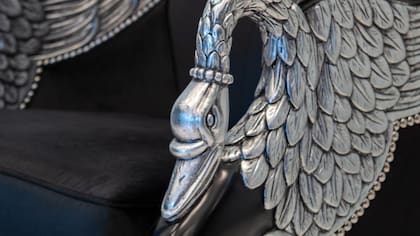 El sillón Cisne tiene apoyabrazos tallados a mano en forma de cisne con acabado en plateado a la hoja.