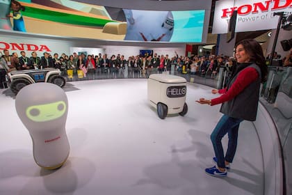 El stand de Honda con su robot de transporte (atrás a la izquierda), el de movilidad personal (el carrito junto a la presentadora) y 3E A18, el robot que intepreta emociones humanas