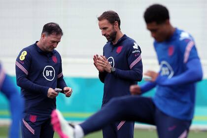 El técnico de Inglaterra, Gareth Southgate (centro) habla con su asistente Steve Holland durante un entrenamiento en Burton upon Trent, el miércoles 30 de junio de 2021 (Nick Potts/PA via AP)