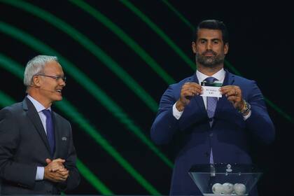 El técnico turco y exjugador Volkan Demirel, derecha, muestra el nombre del club Vaduz durante el sorteo de la Liga Conferencia de la UEFA en Estambul, Turquía, el viernes 26 de agosto de 2022. (AP Foto/Emrah Gurel)
