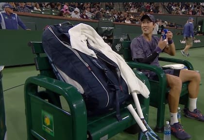 El tenista japonés Yosuke Watanuki, sonriente, pareció pedirle permiso a su equipo para tomar una gaseosa en medio del match