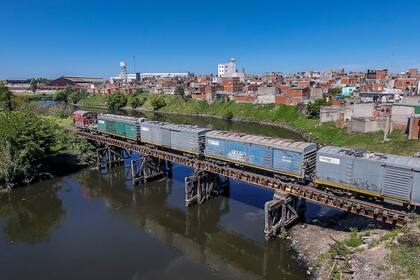 El tren de carga cruza por encima del Riachuelo a través de un puente apoyado sobre columnas de madera gastada