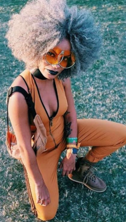 Ella, de afro, overol escotado y anteojos engamados