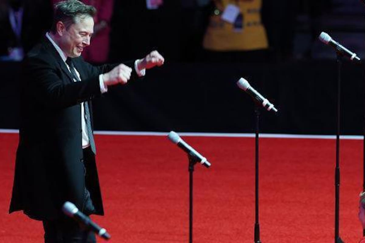 Elon Musk con su hijo, X, en el escenario del mitin de la victoria de Trump en Washington, DC. Musk sonríe y levanta las manos. La cara de X no es visible.