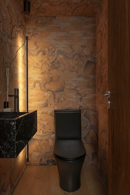 Empapelado ‘Fénix’ (Edición Particular) con textura lienzo y cobertura vinílica. Lavatorio de grafito con grifería monocomando y sanitario ‘Abruzzo’ negro (todo de Lounge Art por Piazza). Aplique de iluminación ‘Stick’ (Boutique de Luz).