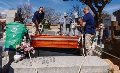 Empleados de un cementerio, protegidos con barbijos, terminan ayer un funeral en el