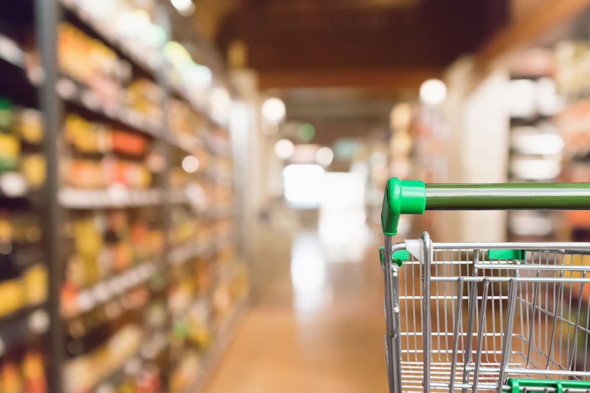Empty green supermarket shopping cart with abstract blur grocery store aisle defocused background