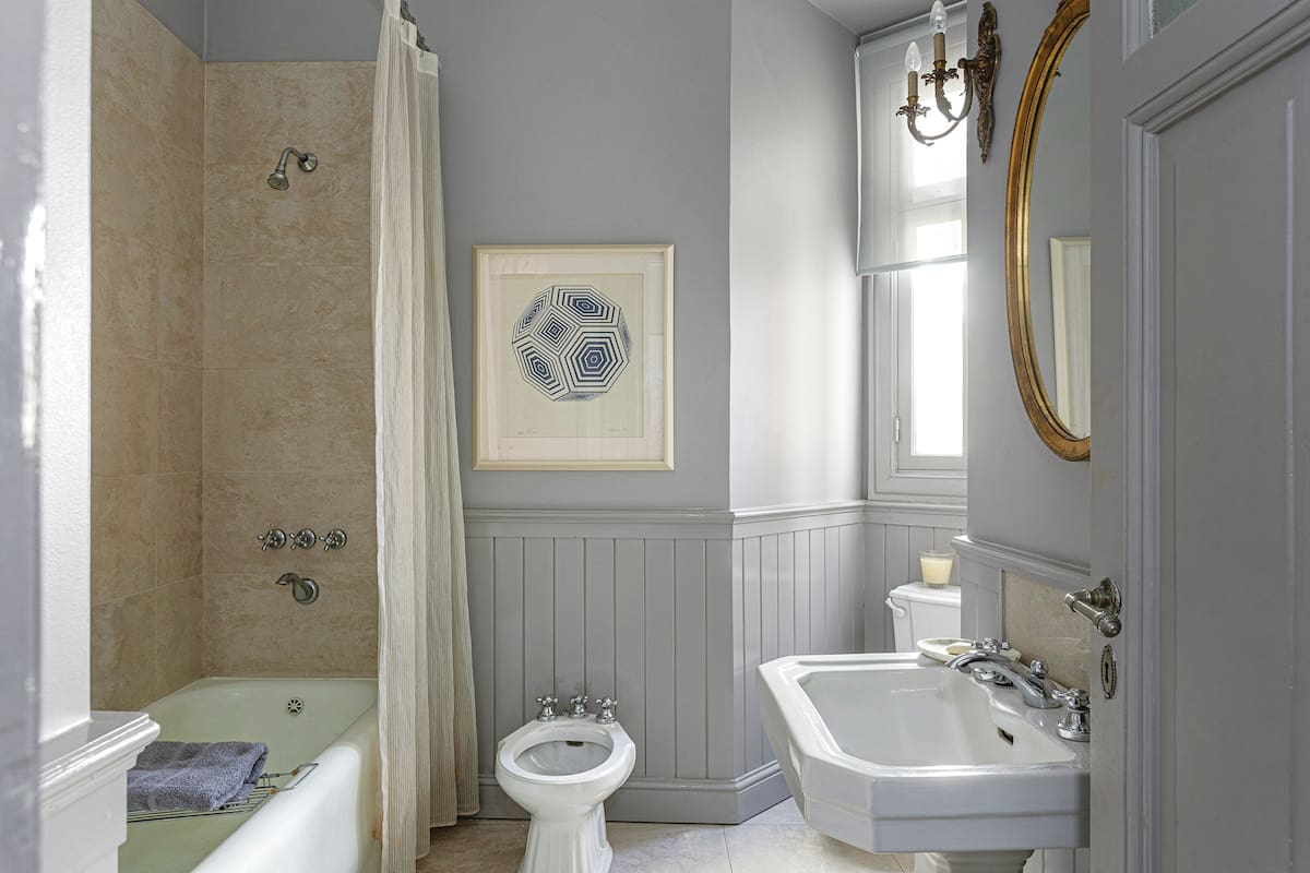 En el baño, artefactos modelo ‘Victoria’ (Ferrum), bañadera original con revestimiento de porcelanato símil Travertino y cortina de organza. Como en la cocina y el comedor diario, machimbre hasta media altura.