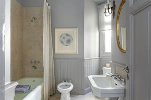En el baño, artefactos modelo ‘Victoria’ (Ferrum), bañadera original con revestimiento de porcelanato símil Travertino y cortina de organza. Como en la cocina y el comedor diario, machimbre hasta media altura.