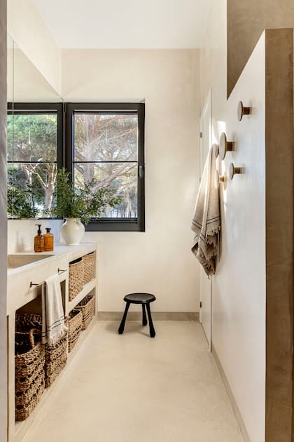 En el baño con muebles de obra, banco de madera (Rue Vintage 74). Perchas para toallas (Muuto). Canastos de mimbre (Mango Home).