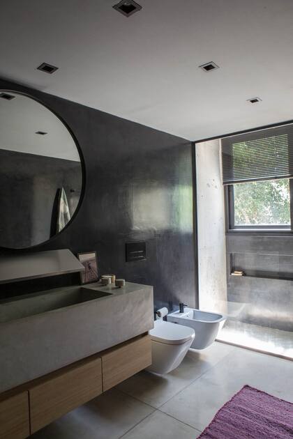En el baño en suite, bacha de hormigón pulido hecha en obra. Vanitory (Cantersfont). Espejo circular (Vetromile Vidrios). Revestimiento en microcemento negro (Quimtex). Sanitarios ‘The Gap’ (Roca).