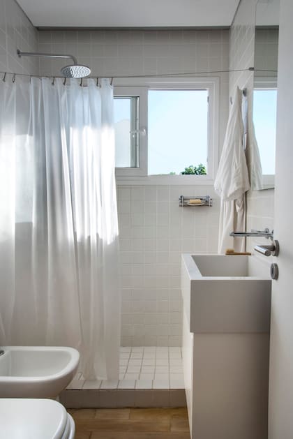 En el baño, revestimiento de cerámicas Pentagres blancas de 5x5. Cortina blanca colgada de un tensor de acero. Vanitory (Mazzinghi-Sánchez Arquitectos) con bacha de apoyo y grifería de pared.