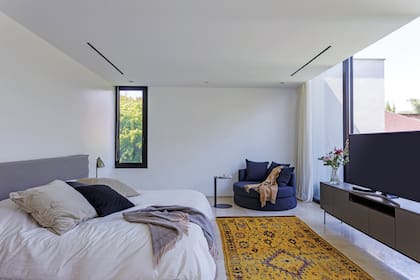 En el dormitorio principal, sillón ‘Pastilla’ (Dharma), alfombra marroquí (Kasbah) y mueble de TV con patas de hierro y estructura laqueada en color visón, a tono con el respaldo de cama, en tussor teñido.