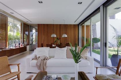 En el living, sofá de tres cuerpos off-white (Vanina Paggi) y sillones individuales heredados y reciclados. Del lado del comedor, lámparas colgantes en chapa de aluminio repujado sostenidas por tensores (Omniluz).