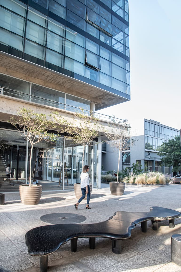 En el Patio Central, el espacio entre los dos edificios, se generó un lugar de espera y de descanso, con bancos “Encuentros” de formas orgánicas, bancos “Rehué” altos y bajos, y maceteros “Canasto”, todos diseños del Estudio Cabeza, con Lagerstroemia indica equilibrando la composición.
