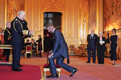 En el salón principal del castillo de Windsor, David Beckham se arrodilla frente al rey Carlos III durante el acto de investidura
