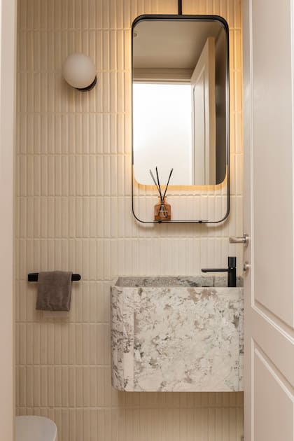 En el toilette, la bacha es de ‘Alpinus White’, elegida en la cantera, con grifería, toallero y luminaria negros. El espejo es un diseño del Estudio y el revestimiento de pared, de Noi Estudio.