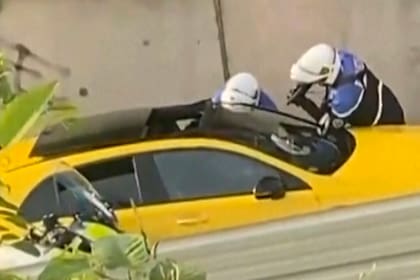 En esta captura tomada de un video proporcionado por @Ohana_FNG, dos policías interrogan a un conductor, uno apuntando con un arma hacia la ventana de un automóvil amarillo, en Nanterre, Francia, el martes 27 de junio de 2023