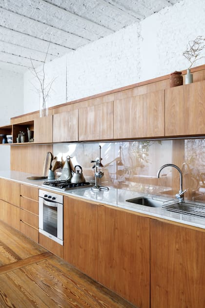 En esta cocina con tanta presencia de la madera, la mitad de la alzada se cubrió con vidrio, para protegerla y facilitar la limpieza.