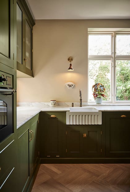 En esta cocina de buscado estilo inglés creada por el Estudio Pernille Lind, variedad de herrajes dorados, incluyendo los clásicos de estilo cubeta, a cada lado de la pileta.