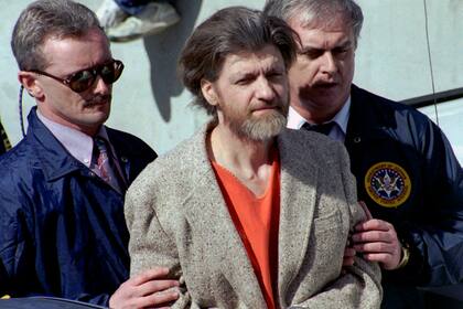 En esta foto de archivo del 4 de abril de 1996, Ted Kaczynski, mejor conocido como Unabomber, está flanqueado por agentes federales mientras lo conducen a un automóvil desde el juzgado federal en Helena