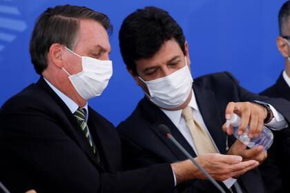 En esta foto de archivo tomada el 18 de marzo de 2020, el presidente brasileño Jair Bolsonaro y su ministro de Salud, Luiz Henrique Mandetta, desinfectan sus manos durante una conferencia de prensa relacionada con el nuevo coronavirus, en el Palacio de Planalto en Brasilia