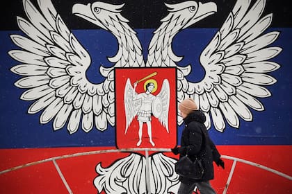 En esta foto de archivo tomada el 19 de enero de 2022, un peatón pasa junto a un enorme emblema estatal de la autoproclamada República Popular de Donetsk (RPD) en Donetsk, este de Ucrania.