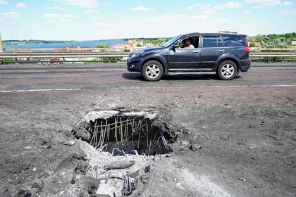 En esta foto de archivo tomada el 21 de julio de 2022, un coche pasa por delante de un cráter en el puente Antonivskyi, que cruza el río Dniéper de Kherson, causado por un ataque ucraniano con cohetes, en medio de la actual acción militar rusa en Ucrania.