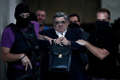 En esta foto de archivo tomada el 28 de septiembre de 2013, el líder del partido de ultraderecha Amanecer Dorado, Nikos Michaloliakos, es escoltado por agentes de policía enmascarados hasta el fiscal desde la sede de la policía en Atenas