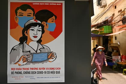 En esta foto de archivo tomada el 29 de abril de 2020, se ve un cartel de propaganda sobre la prevención de la propagación del nuevo coronavirus en una pared mientras una mujer pasa caminando por una calle en Hanoi