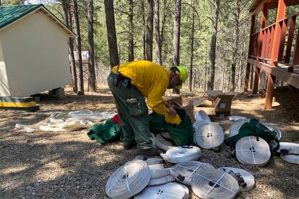 En esta foto difundida por el Servicio Forestal de Estados Unidos, un bombero reúne mangueras y accesorios para montar sistemas de protección por aspersión en el Bosque Nacional de Santa Fe en Nuevo México el jueves 28 de abril de 2022. (J. Michael Johnson/Servicio Forestal de Estados Unidos vía AP)