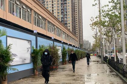 En esta foto tomada el 24 de noviembre de 2020, personas que usan mascarillas como medida preventiva contra el coronavirus caminan junto al mercado mayorista de mariscos de Huanan en Wuhan, en la provincia central china de Hubei