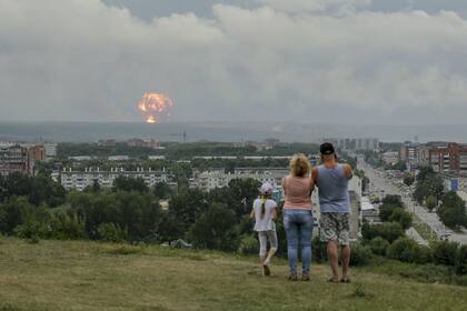 En esta foto tomada el lunes 5 de agosto de 2019, una familia observa explosiones en un depósito militar de municiones cerca de la ciudad de Achinsk, en la región de Krasnoyarsk, en el este de Siberia