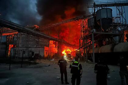 En esta fotografía proporcionada por el jefe de gabinete presidencial de Ucrania, Andriy Yermak, el 28 de agosto de 2023, agentes del orden público ucranianos están junto a la instalación industrial en llamas después de un ataque con misiles en la aldea de Hoholeve, región de Poltava.