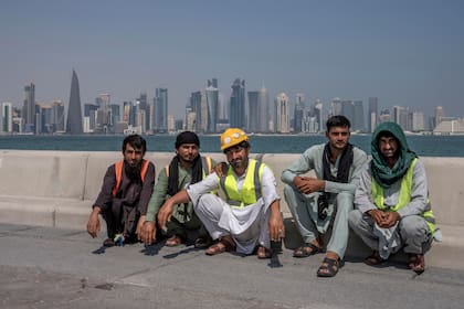 En esta imagen de archivo, trabajadores migrantes paquistaníes posan para una fotografía durante un descanso en su jornada laboral, en el paseo marítimo, con vistas al perfil de la ciudad de Doha, en Qatar, el 19 de octubre de 2022. (AP Foto/Nariman El-Mofty, archivo)