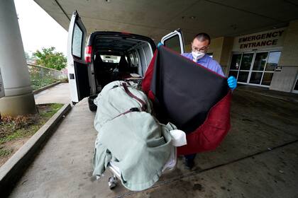 En esta imagen del 18 de agosto de 2021, el empleado de una funeraria local cubre el cuerpo de un paciente de COVID-19 que perdió la vida, mientras lo prepara para trasladarlo a la zona de carga, en el Centro Médico Willis-Knighton de Shreveport, Luisiana. (AP Foto/Gerald Herbert, Archivo)