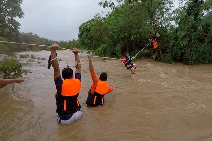 En esta imagen, distribuida por la agencia de gestión de desastres municipal de Gonzaga, un residente avanza por una cuerda mientras rescatistas esperan al otro lado de un río cuyo caudal aumentó notablemente por las fuertes lluvias de la tormenta tropical Kompasu, en Gonzaga, en la provincia de Cagayan, en el norte de Filipinas, el 11 de octubre de 2021. (Gonzaga MDRRMO vía AP)