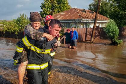 En esta imagen, distribuida por los servicios de emergencia de Rumanía, ISU Galati, un rescatista carga con una mujer a la espalda en una zona inundada en Pechea, Rumanía, el 14 de septiembre de 2024, tras las lluvias torrenciales que dejaron decenas de personas varadas. (Servicios de Emergencia de Rumanía, ISU Galati vía AP)