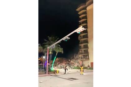 En esta imagen extraída de un video, equipos de bomberos en el lugar un edificio derruido en Surfside, Miami, Florida, el jueves 24 de junio de 2021. El derrumbe parcial de un edificio en Miami provocó un gran despliegue de servicios de emergencias, según el servicio de bomberos de Miami Dade. (Jamal Akakpo via AP)