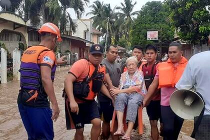 En esta imagen proporcionada por la Guardia Costera de las Filipinas, una anciana es transportada sobre una silla por personal del servicio de guardacostas en medio de una inundación, el lunes 26 de diciembre de 2022, en Plaridel, en el sur de las Filipinas. (Guardia Costera de las Filipinas vía AP)