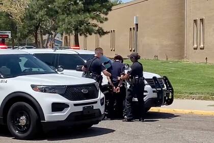En esta imagen tomada de un video, cortesía de Ryan Laughlin/KOB 4 TV, agentes del Departamento de Policía de Albuquerque registran a un alumno el viernes 13 de agosto de 2021 después de un tiroteo en la Escuela Secundaria Washington. Un estudiante murió y otro fue detenido, según la policía. (Ryan Laughlin/KOB 4 TV vía AP)