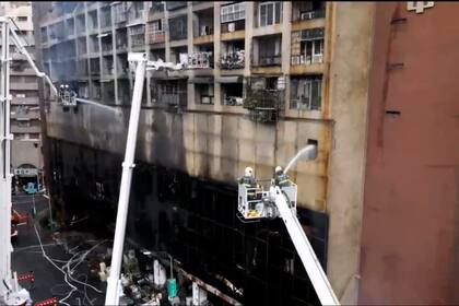 En esta imagen tomada de un video del medio taiwanés EBC, bomberos lanzando agua a un edificio incendiado en Kaohsiung, en el sur de Taiwán, el jueves 14 de octubre de 2021.  (EBC via AP )